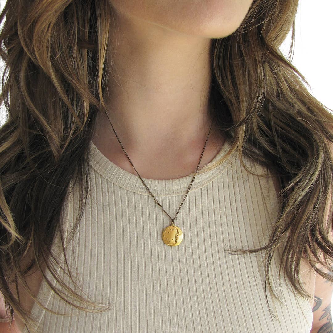 Close-up of a person wearing a gold necklace with a coin pendant.