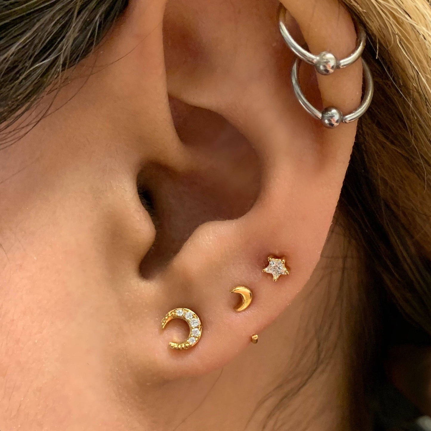 Close-up of an ear with gold and silver earrings.
