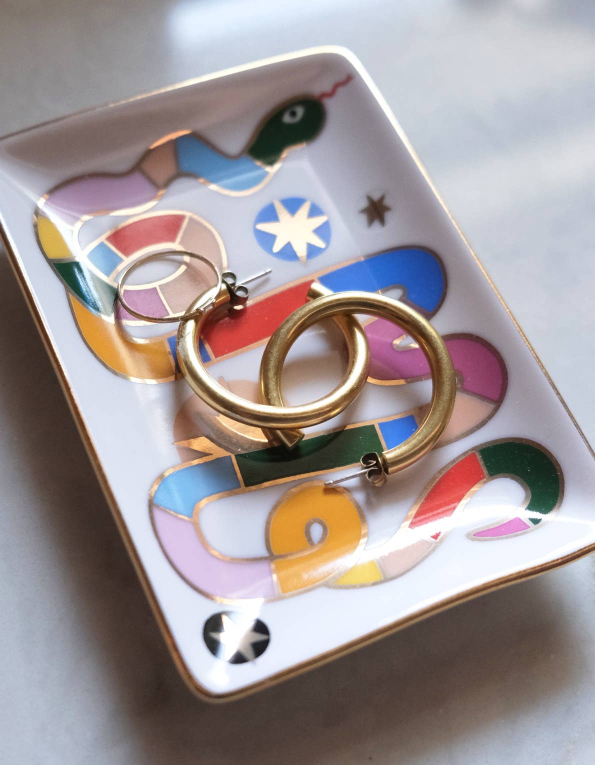 Gold hoop earrings on a colorful ceramic dish with abstract designs