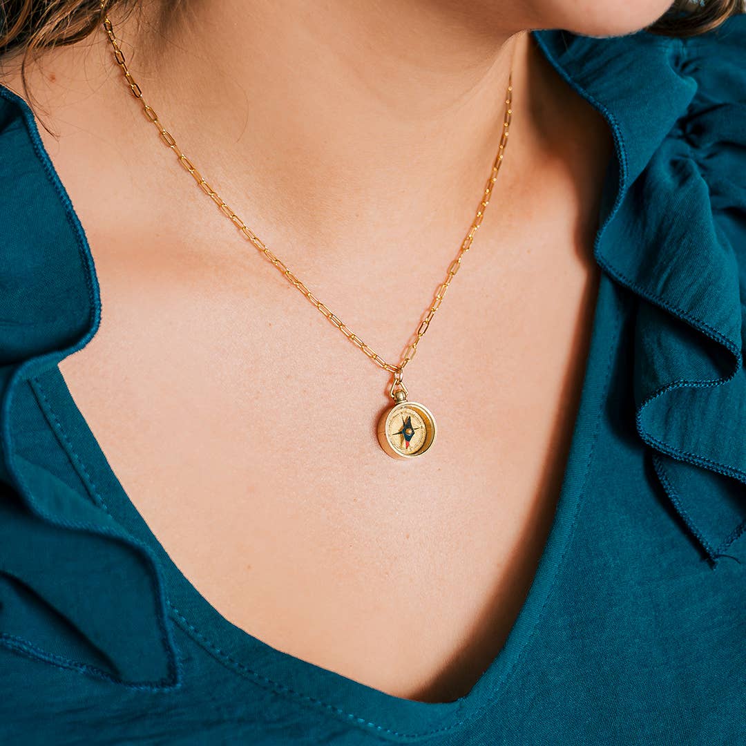 Gold necklace with a pendant worn by a person in a blue top