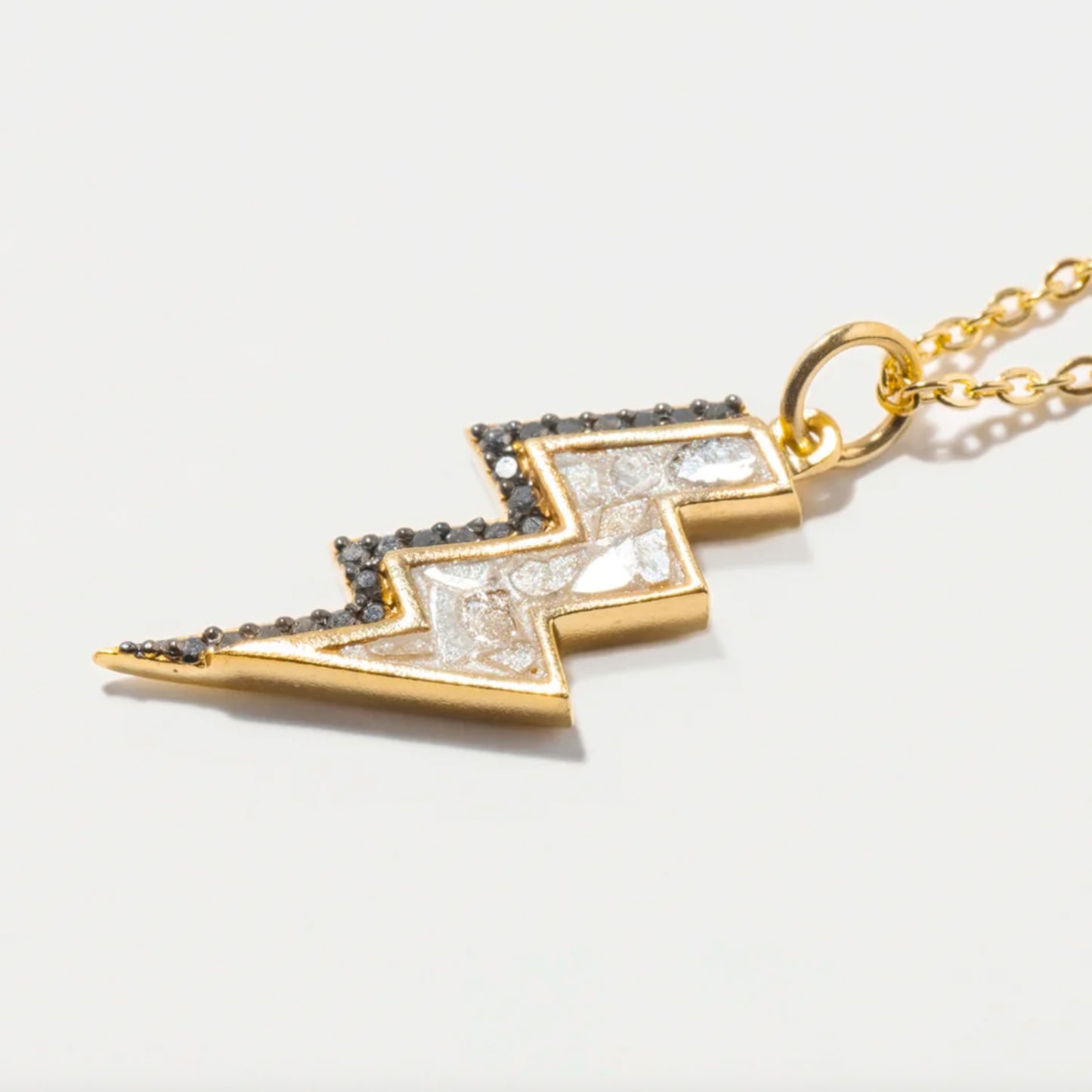 Gold lightning bolt pendant with black and clear stones on a light gray background