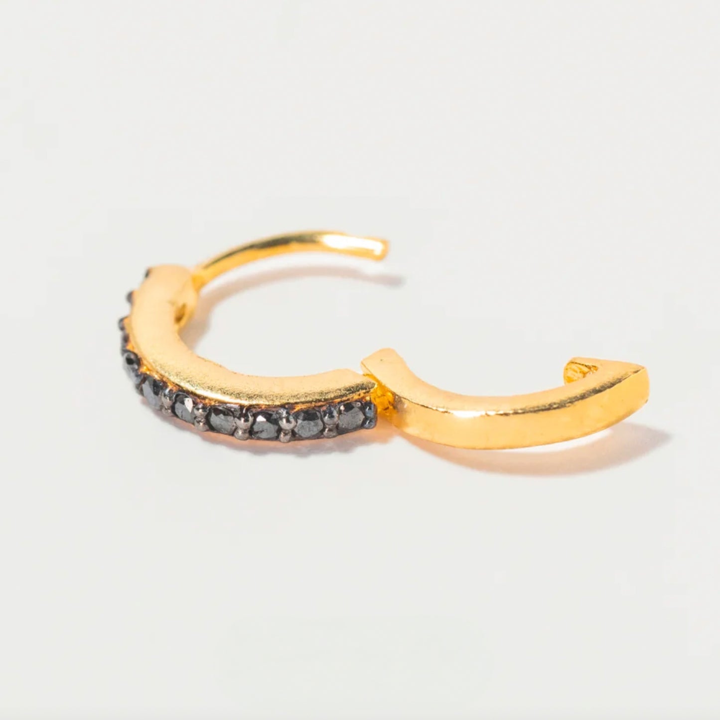 Gold hoop earring with embedded stones on a light gray background