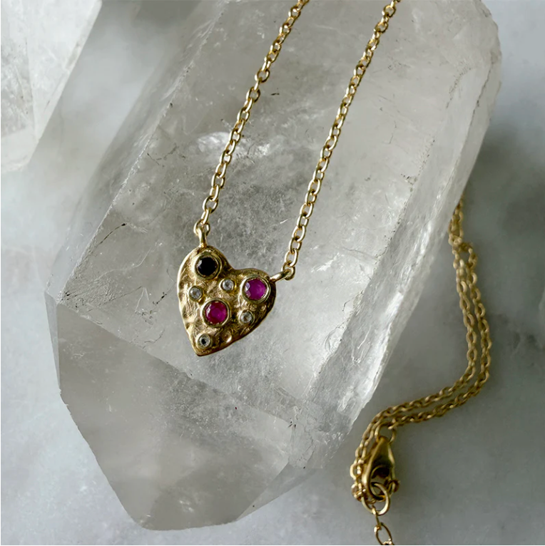 Gold heart-shaped necklace with gemstones on a crystal background