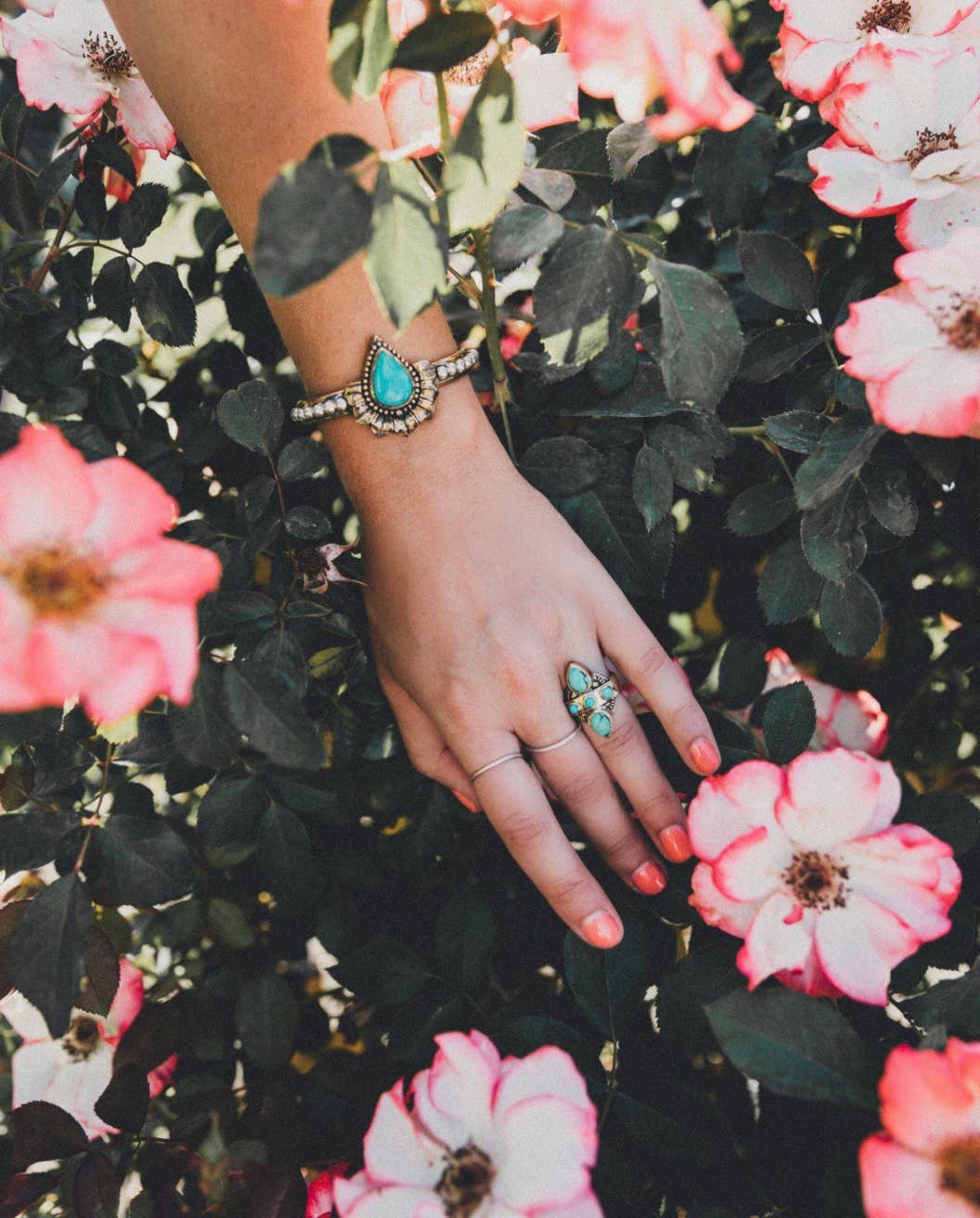 Hand with turquoise jewelry on a background of pink flowers