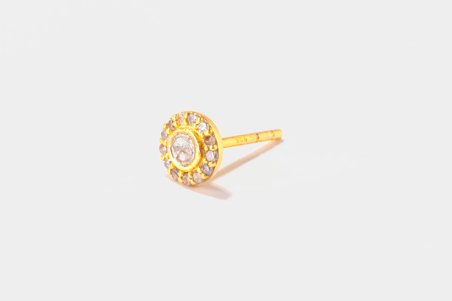Gold earring with a central gemstone on a light gray background
