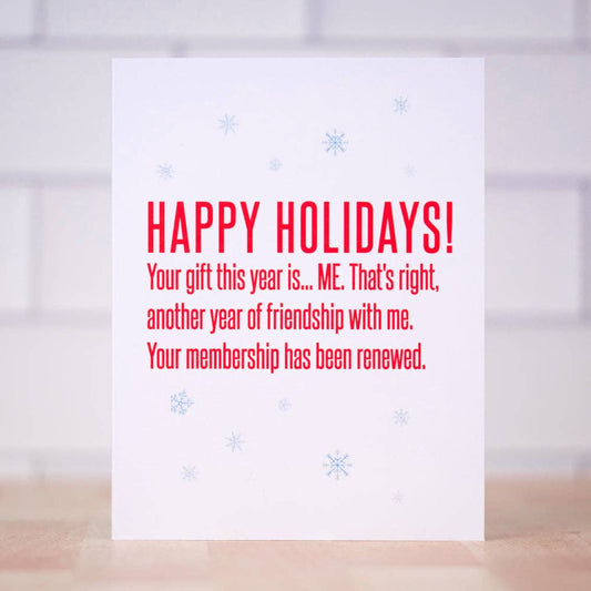 A white greeting card with red text reading 'HAPPY HOLIDAYS! Your gift this year is.