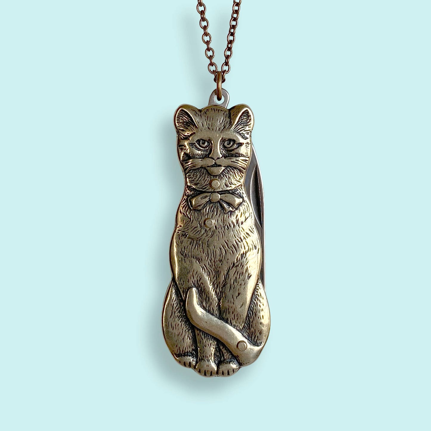 Metallic cat-shaped pendant a chain on a light gray background