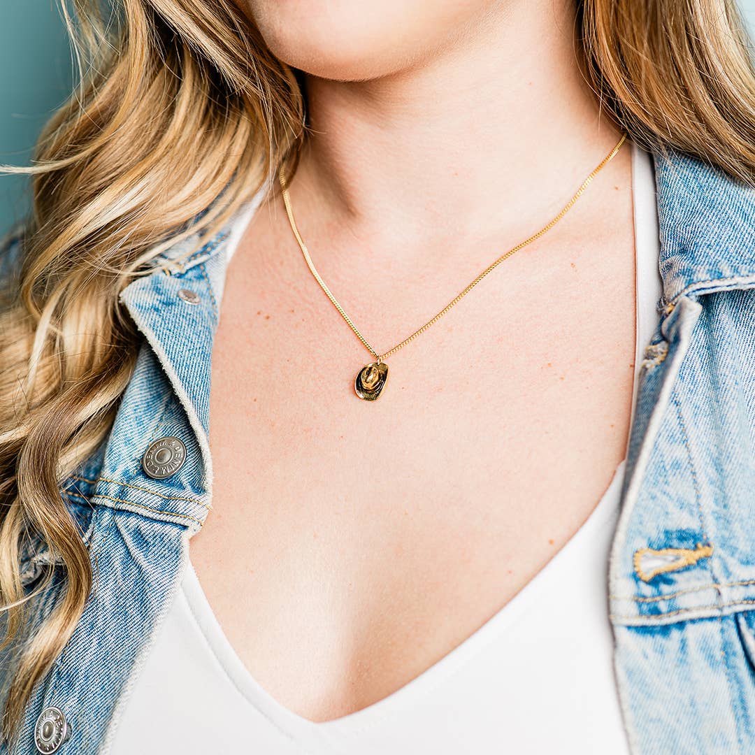 Person wearing a gold necklace with a pendant, dressed in a denim jacket and white top.