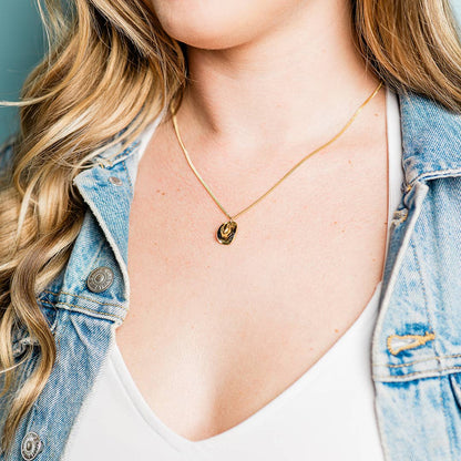 Person wearing a gold necklace with a pendant, dressed in a denim jacket and white top.