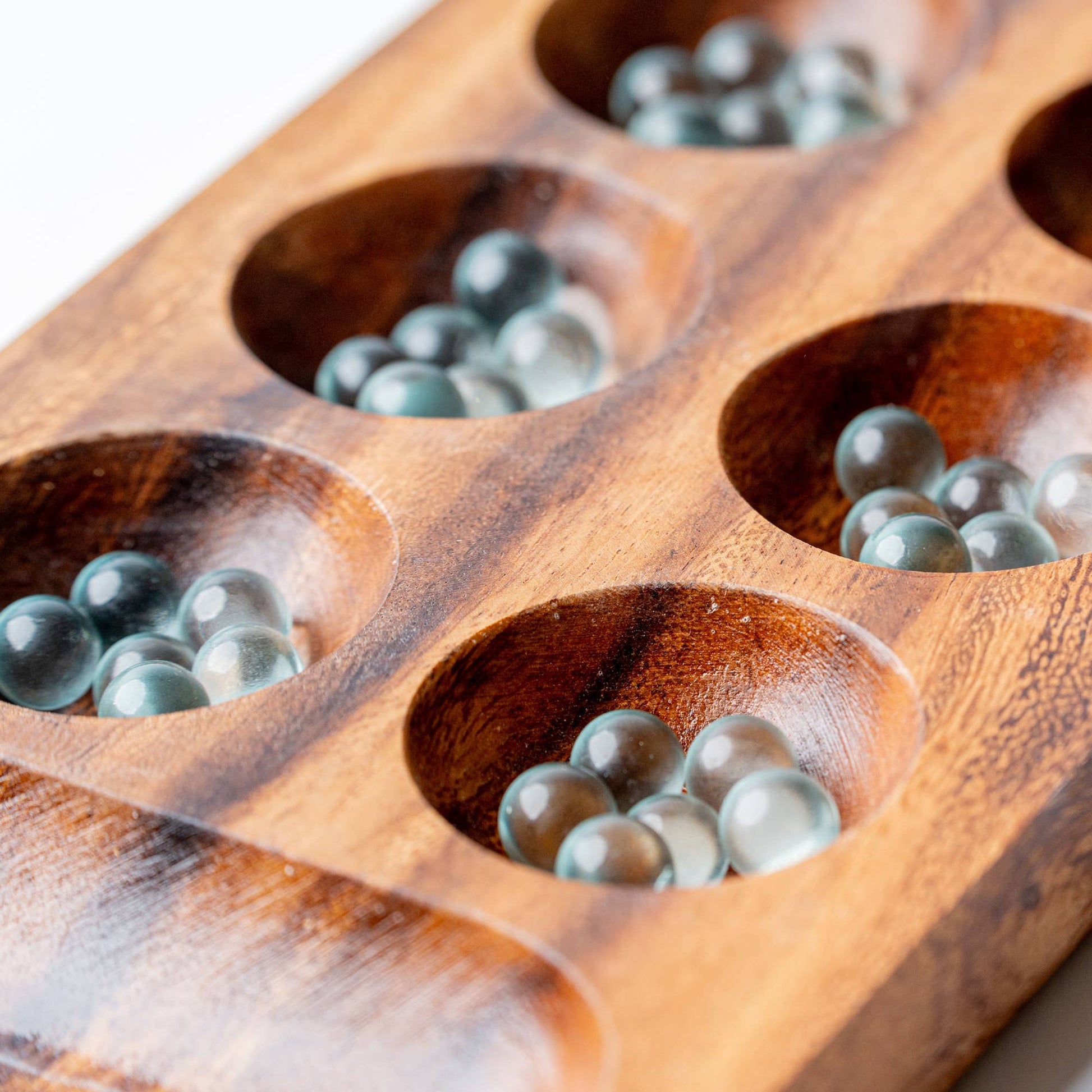 Wooden game board with compartments filled with clear marbles on a wooden surface.