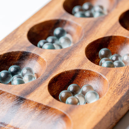 Wooden game board with compartments filled with clear marbles on a wooden surface.