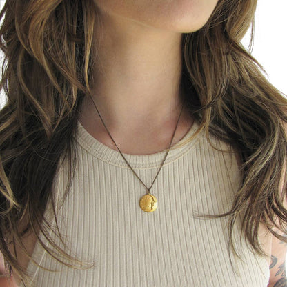 Close-up of a person wearing a gold necklace with a coin pendant.