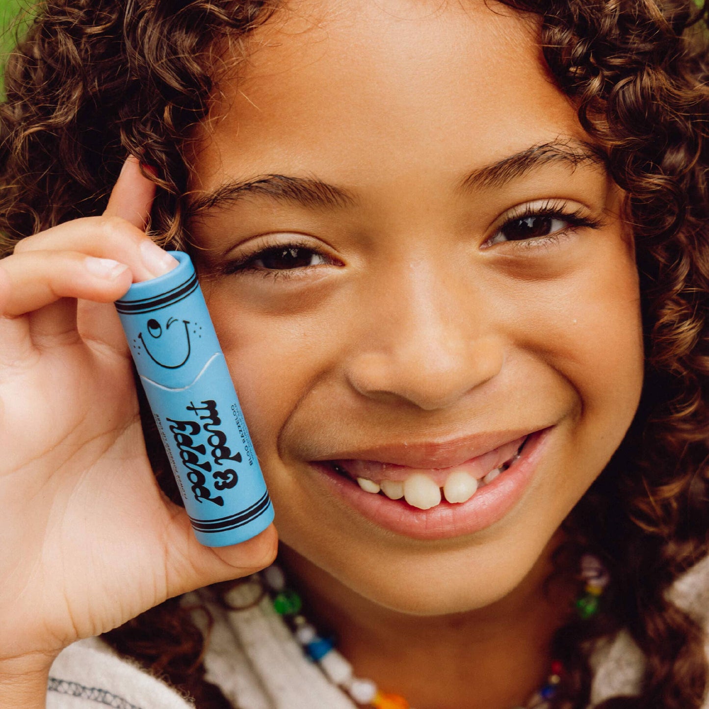 Child holding a blue tube of lip balm with a smiley face, smiling at the camera.