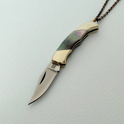 Decorative knife pendant with a chain on a light gray background