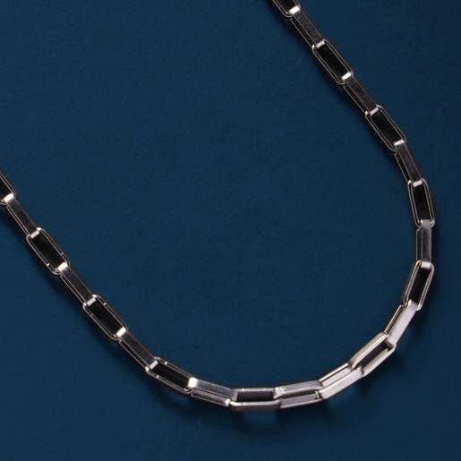 A silver-toned paperclip chain necklace displayed in a curved shape against a dark blue textured background.