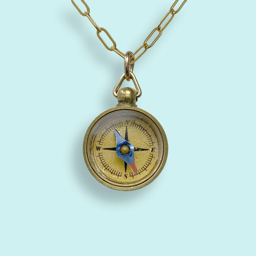 Gold compass pendant on a chain against a light blue background