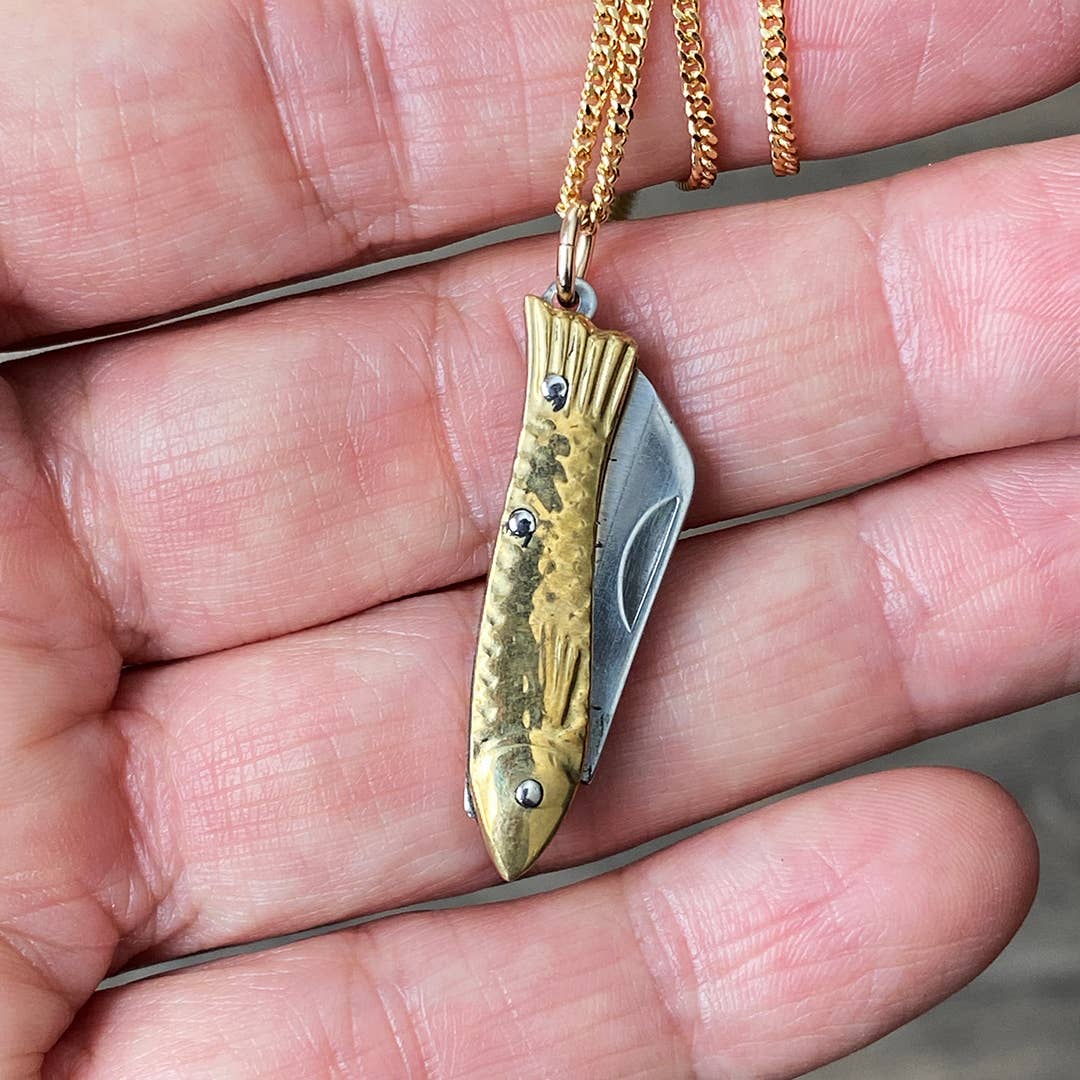 Gold and silver fish-shaped pendant on a chain held in a hand.