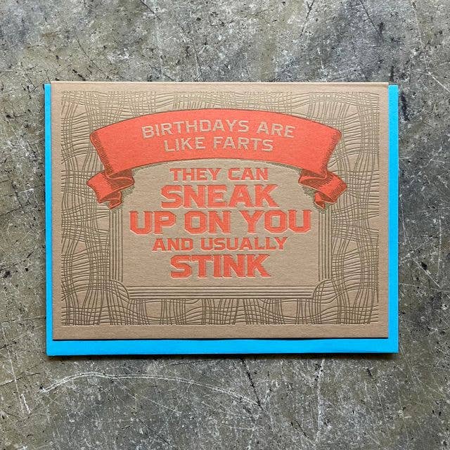 A square greeting card with a humorous birthday message, displayed flat on a textured gray concrete surface. The card has a brown kraft-paper background with a red banner and red text that reads 'BIRTHDAYS ARE LIKE FARTS THEY CAN SNEAK UP ON YOU AND USUALLY STINK'.