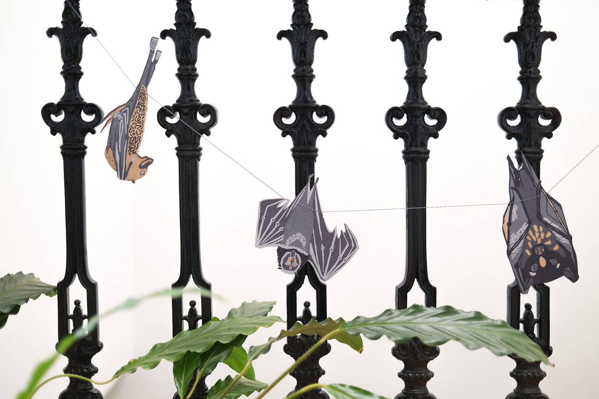 Decorative bats hanging on a black metal fence with green leaves in the foreground.
