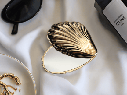 Gold shell-shaped jewelry dish on a white fabric background with Celine handbag partially visible.