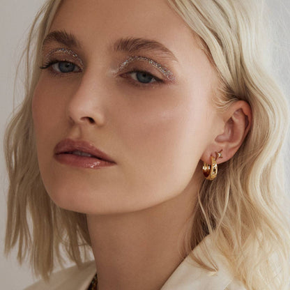 Close-up of a woman with blonde hair and gold hoop earrings against a neutral background