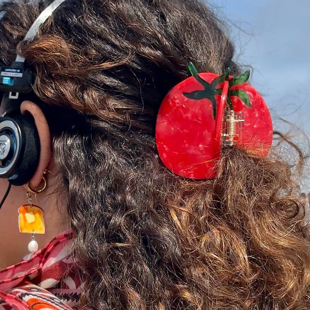Close-up of a person's hair with a red tomato-shaped hair clip and headphones.