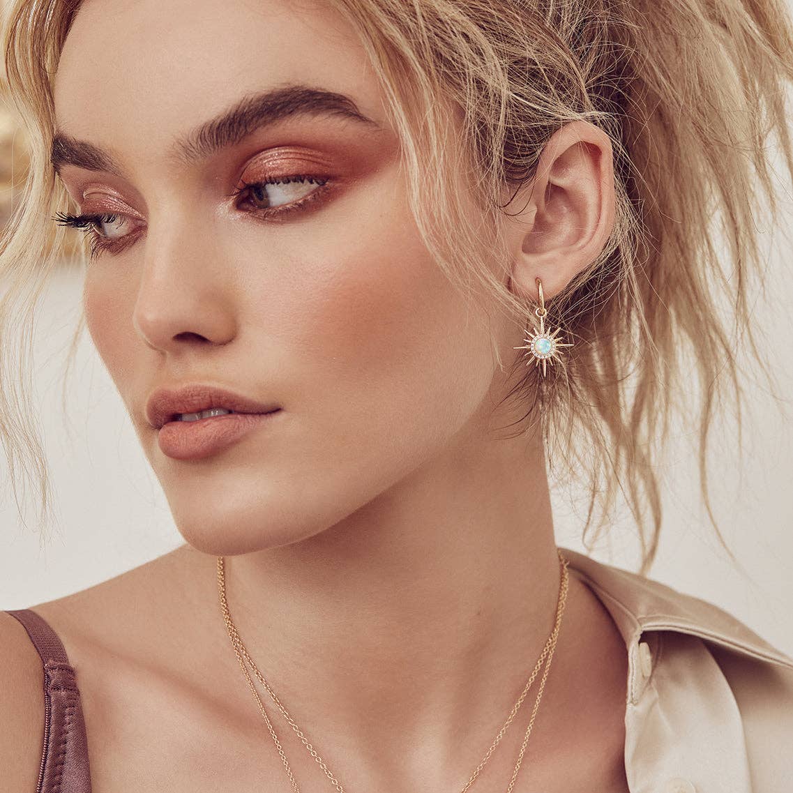 Close-up of a woman wearing gold earrings and a necklace with a neutral background