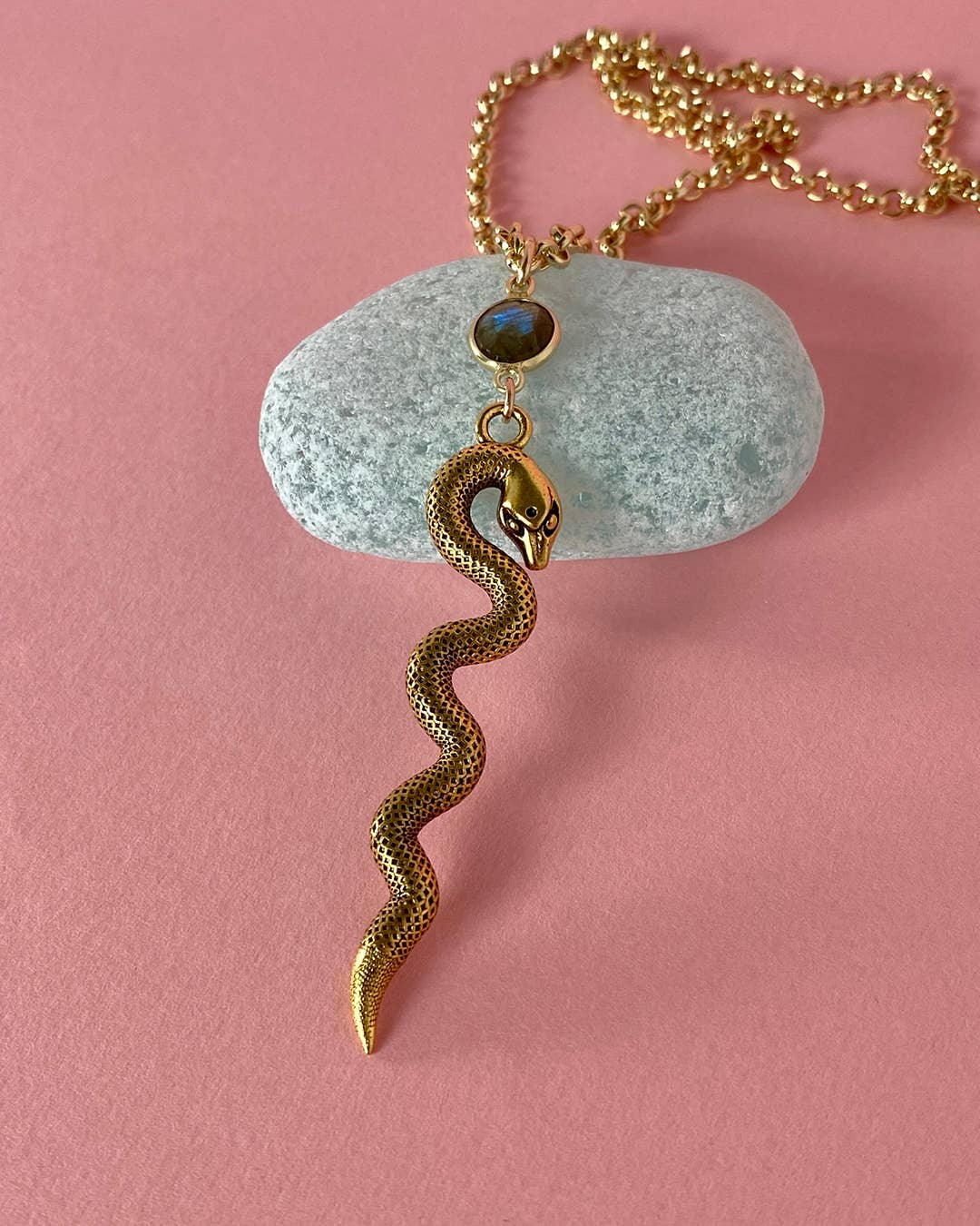 Gold snake pendant necklace on a pink background