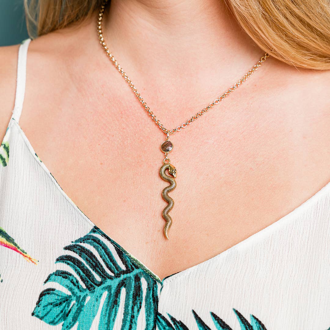 Necklace with a snake pendant worn by a person in a white top with green leaf patterns.
