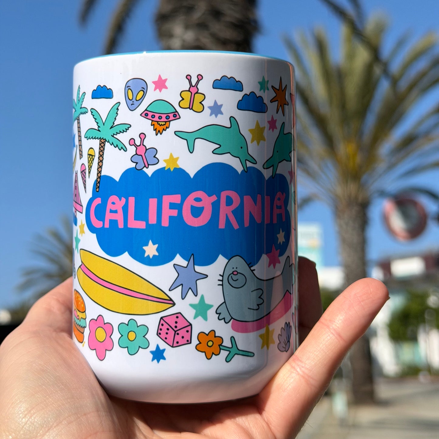 Colorful mug with 'California' design held in front of palm trees