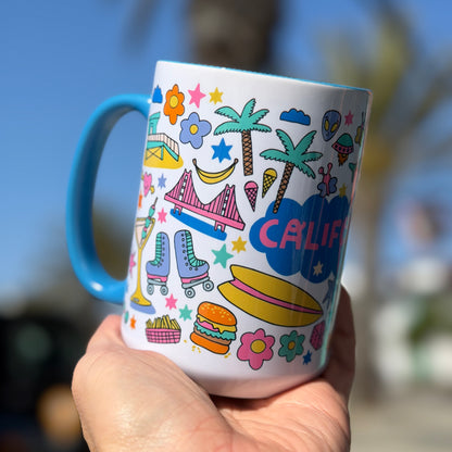 Mug with colorful California-themed design held in a hand against a blurred outdoor background