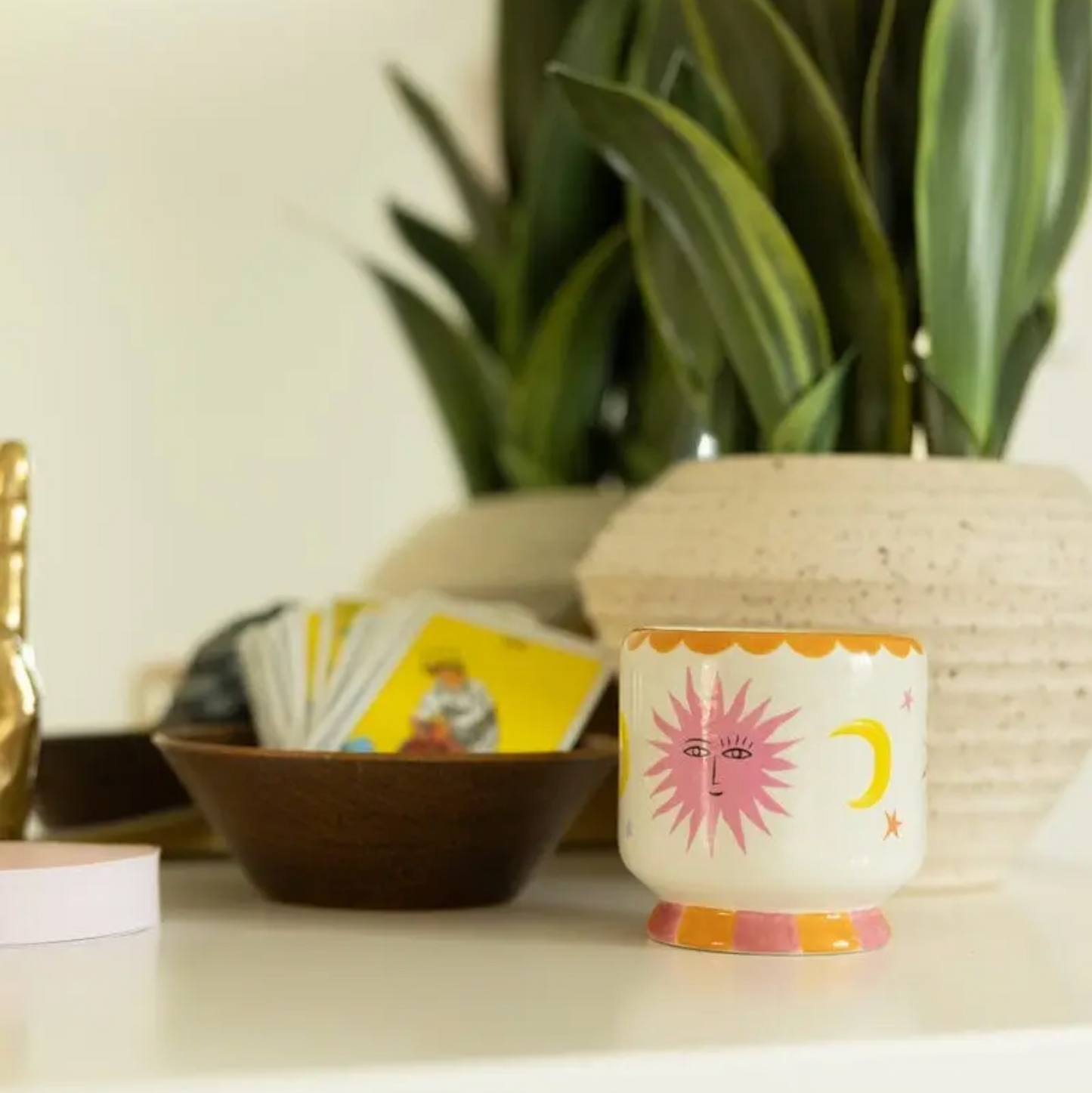 Decorative candle with sun and moon design on a surface with plants and cards in the background