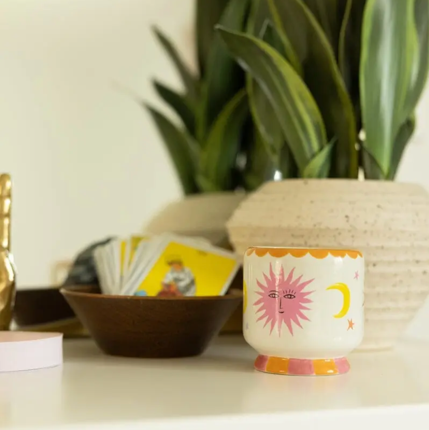 Decorative candle with sun and moon design on a surface with plants and cards in the background