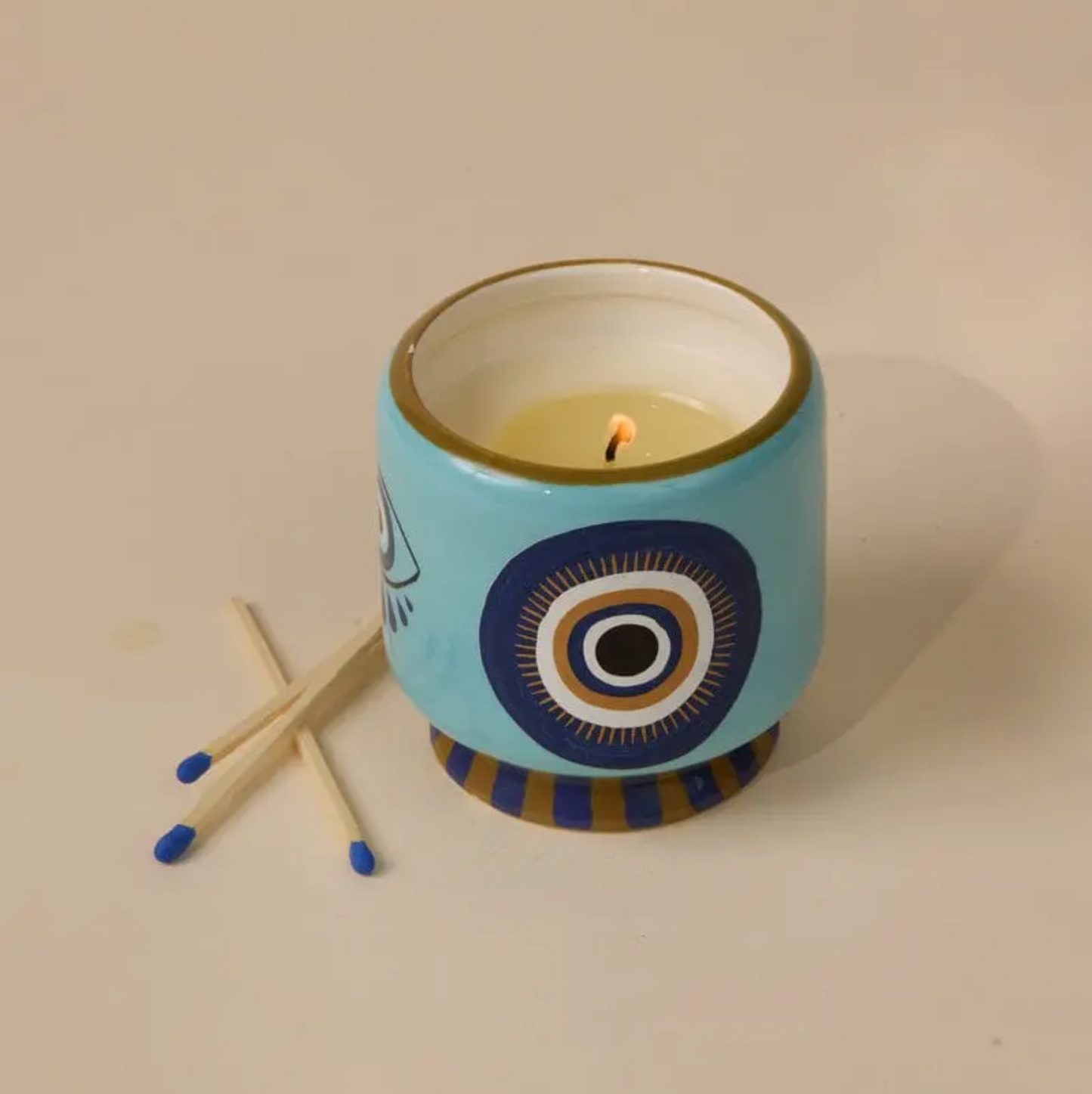 Candle in a decorative blue holder with matches on a beige background