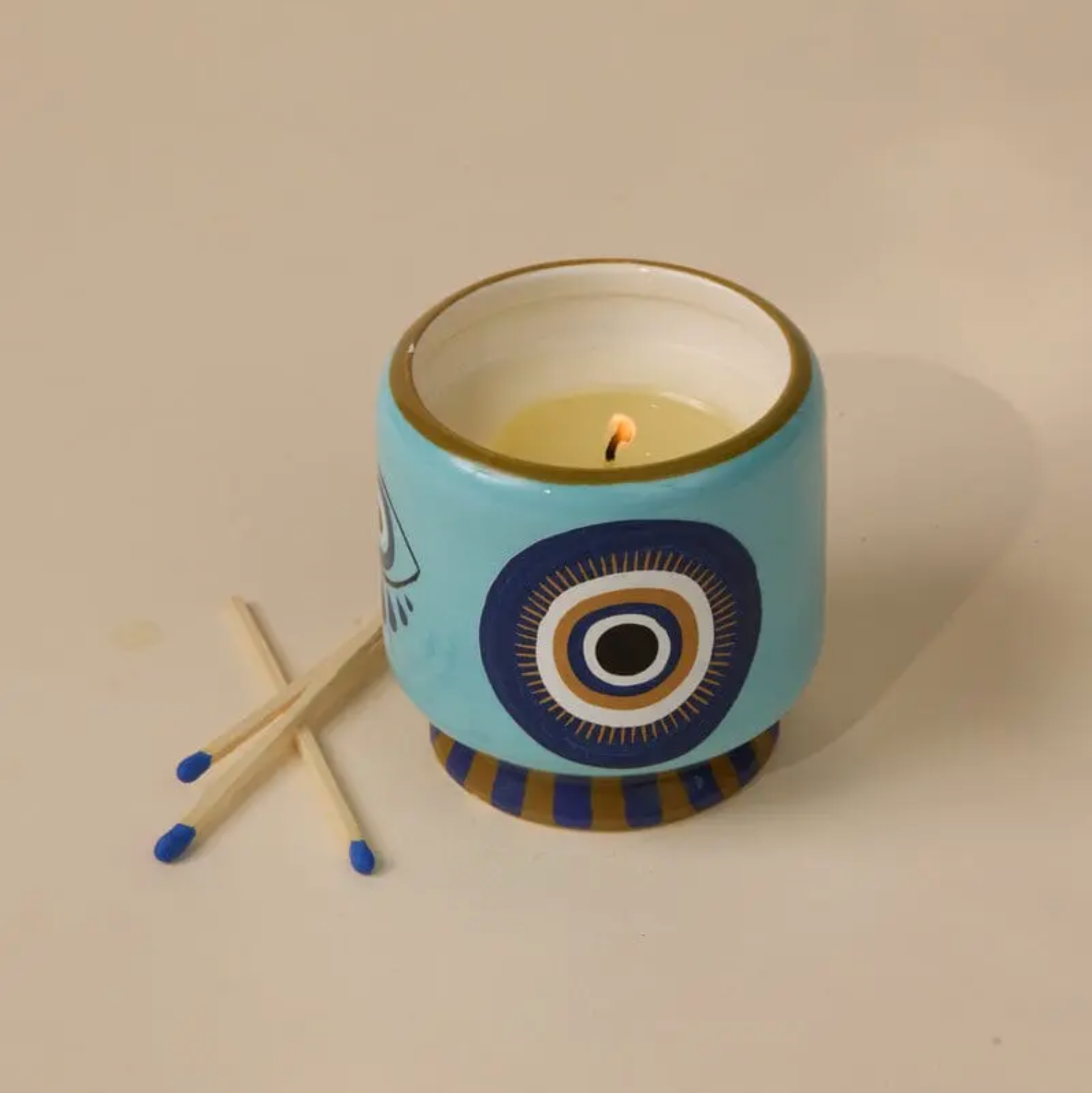 Candle in a decorative blue holder with matches on a beige background