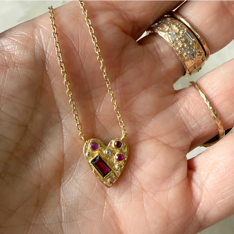 Gold heart-shaped necklace with gemstones held in a hand.