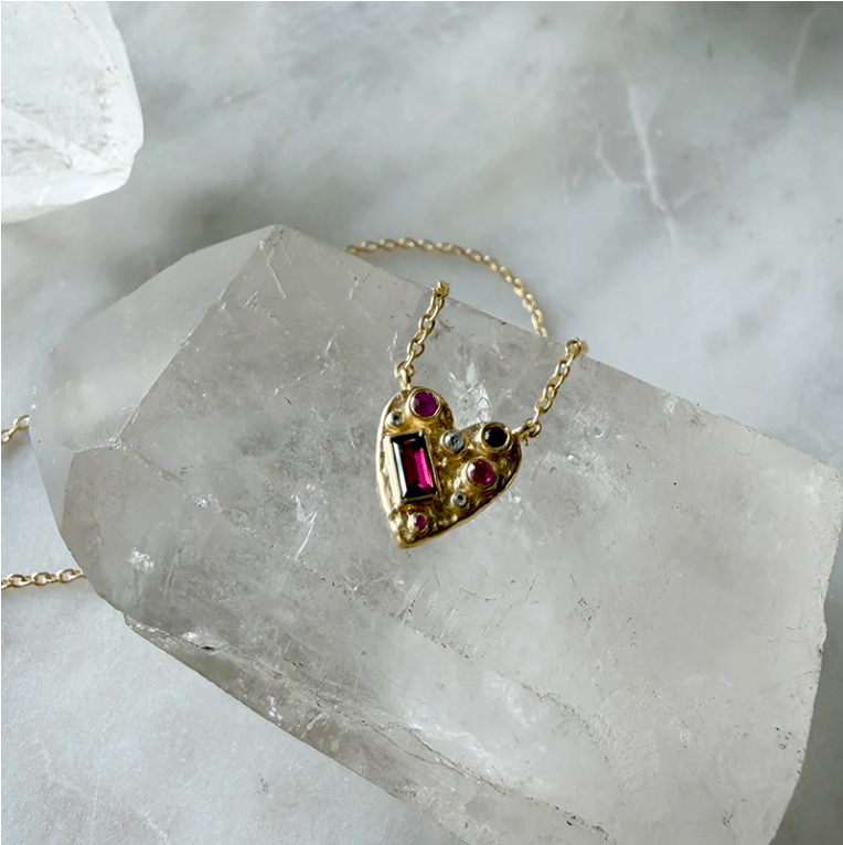 Gold heart-shaped necklace with gemstones on a crystal surface