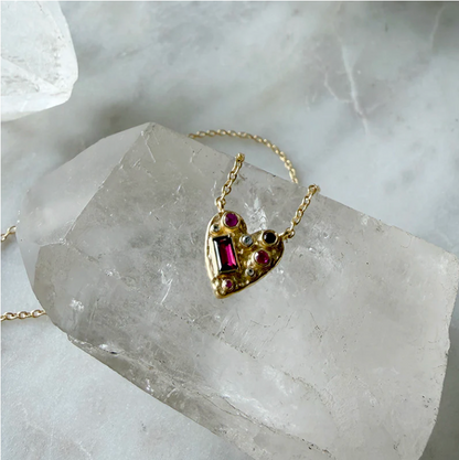 Gold heart-shaped necklace with gemstones on a crystal surface