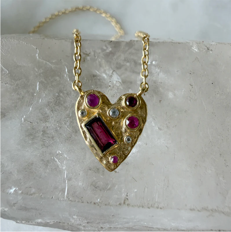 Heart-shaped gold pendant with embedded gemstones on a marble surface