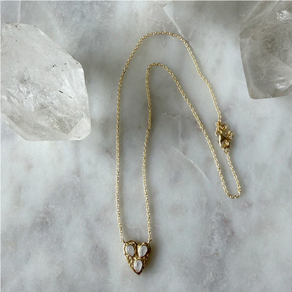 Gold necklace with a heart-shaped pendant on a marble surface