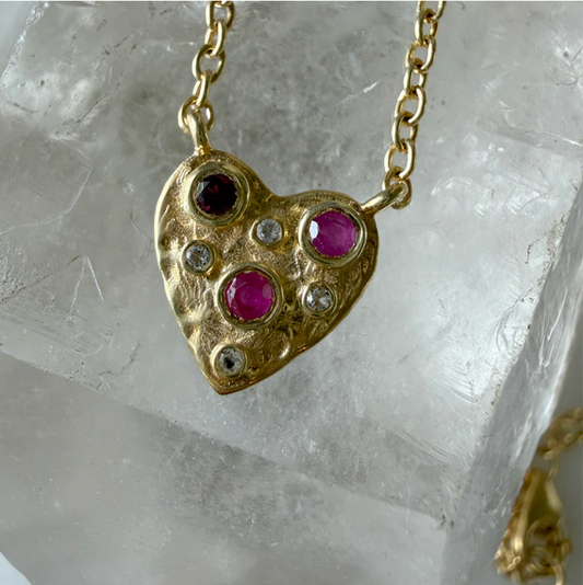 Gold heart-shaped necklace with gemstones on a crystal background