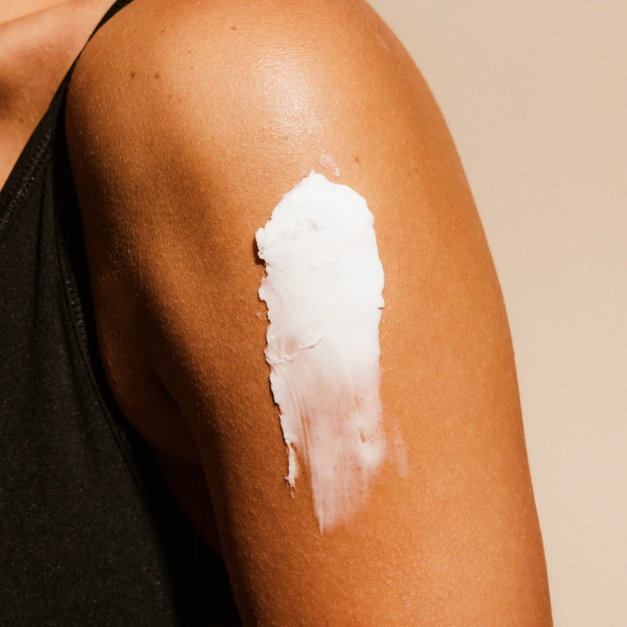 White body butter cream applied to a person's shoulder on a beige background