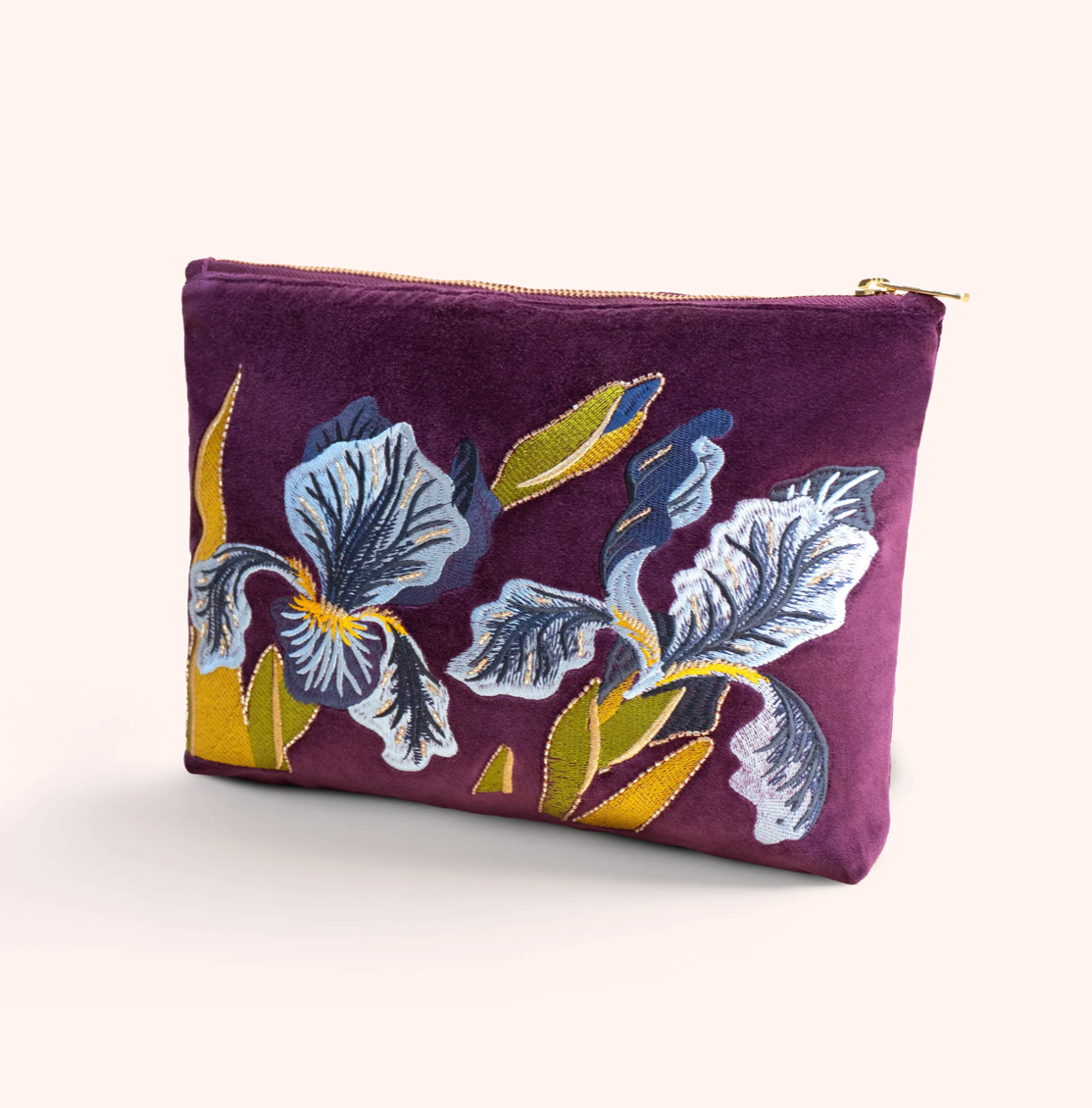 A purple velvet zippered pouch featuring a large embroidered iris floral design in blue, white, and yellow, set against a plain light beige background.