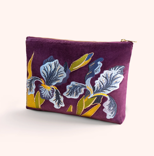 A purple velvet zippered pouch featuring a large embroidered iris floral design in blue, white, and yellow, set against a plain light beige background.