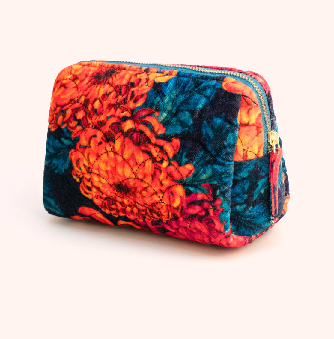 A small zippered cosmetic pouch with a vibrant floral print in orange, red, and teal, shown on a solid pale pink background.