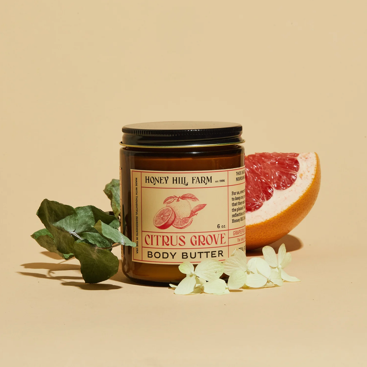 Jar of Honey Hill Farm Citrus Grove Body Butter with a grapefruit and leaves on a beige background