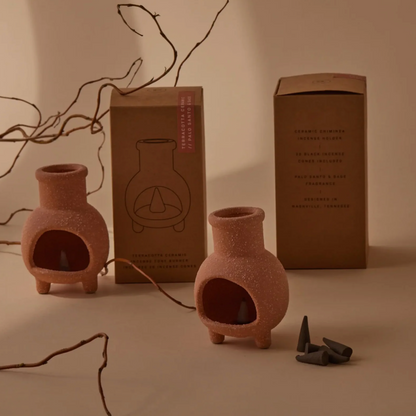 Two terracotta-colored ceramic incense burners with a textured finish, shown alongside their brown cardboard packaging boxes and a few dark incense cones on a warm beige background with decorative branches.