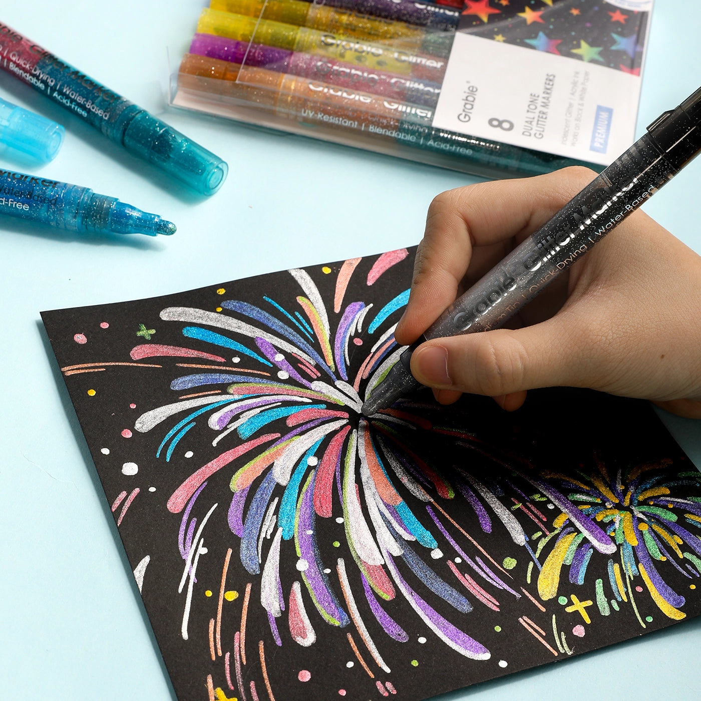 Hand drawing a colorful firework design on black paper with markers.