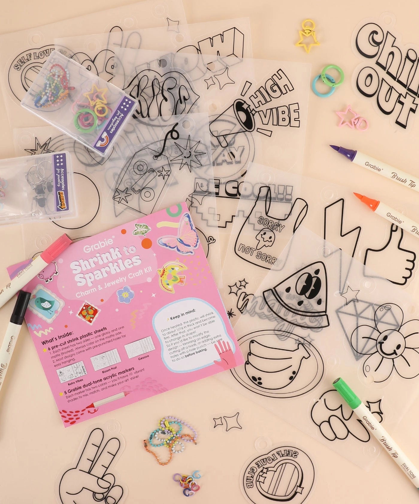 Collection of shrinky dinks, markers, and a pink manual on a beige background
