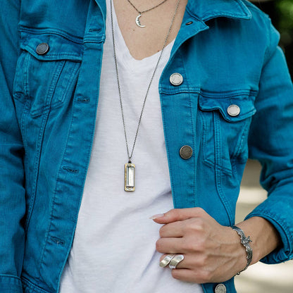 Person wearing a blue jacket and white shirt with jewelry, including a necklace and rings.